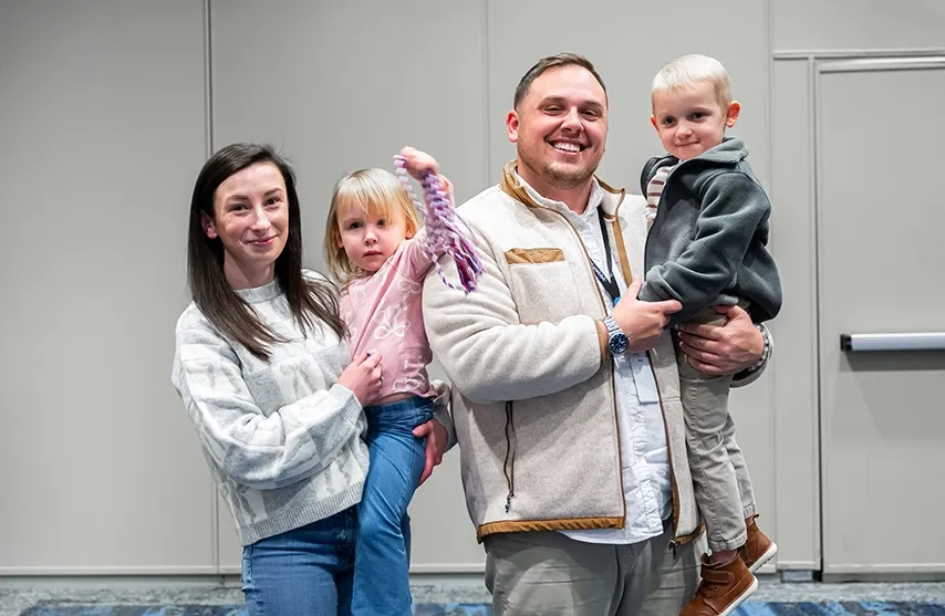 Kara DeBaker, her husband, and two kids smile at the camera.